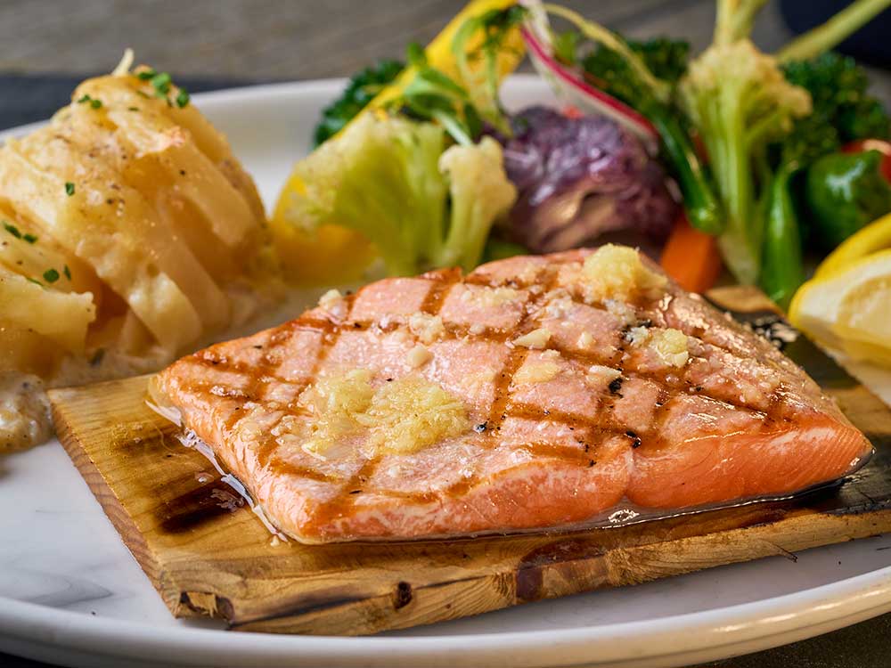 Grilled salmon on wood serving tray surrounded by vegetables